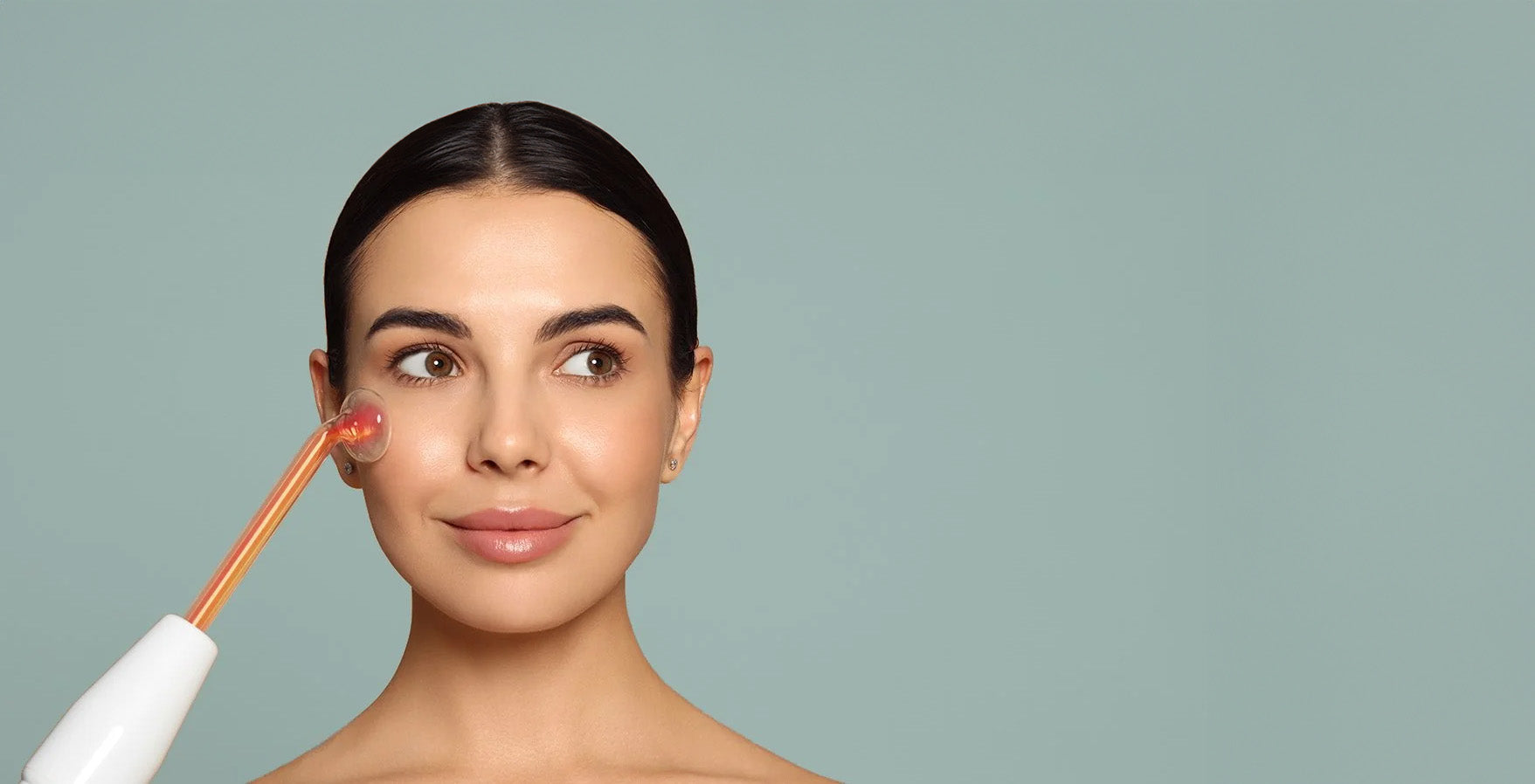 Woman applying cream to her face with a brush against a plain background